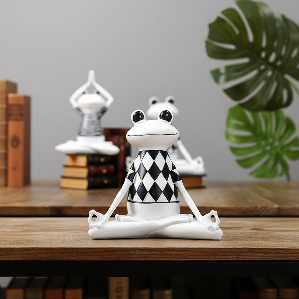 Wichtelgeschenke Idee: weisse Frosch-Figur im Yoga-Sitz mit Rautenmuster auf Holztisch vor Büchern und Monstera
