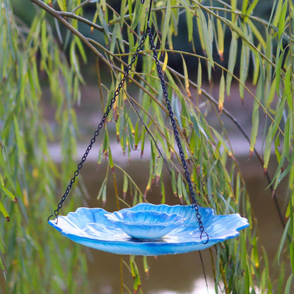 Glasschale Vogelfutterstation in Hellblau hängt an Trauerweidenzweigen über einem Teich