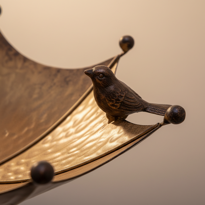 Detailaufnahme der kleinen Vogelfigur aus Bronze am Rand des umgedrehten Regenschirm-Futterspenders