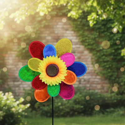 Windrad Sonnenblume mit bunten Pailletten-Blättern vor efeubewachsener Ziegelmauer im warmen Sonnenlicht