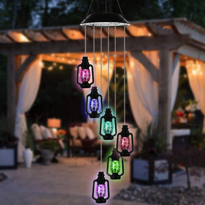 Solar Windspiel mit sechs hängenden Laternen in Pink, Blau und Grün an einer Pergola vor beleuchteter Lounge am Abend