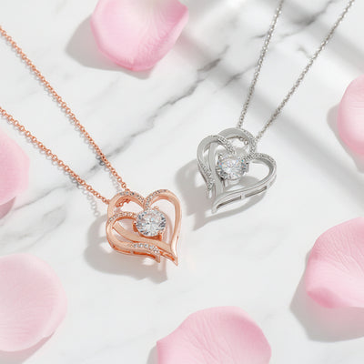 Herz Halskette in Roségold und Weissgold mit Zirkonia, zarter Schmuck auf Marmor zwischen rosa Rosenblättern