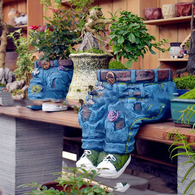 Jeans Blumentopf sitzend mit Turnschuhen auf einer Holzbank, bepflanzt mit Rosen und Pflanzen