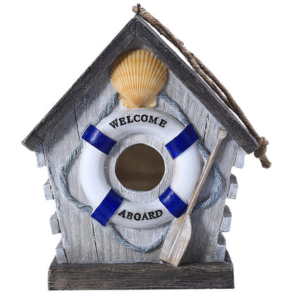 Maritimes Vogelhaus mit Welcome-Aboard-Rettungsring und Paddel auf dunklem Sockel