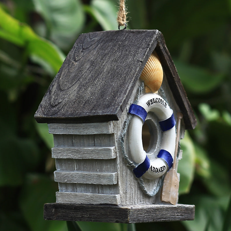 Vogelhäuschen aus Kunstharz hängt an einem Ast im grünen Garten zwischen Blättern