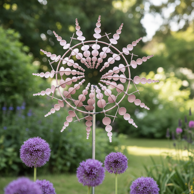 Windrad für den Garten aus Metall in Rosé und Silber dreht sich zwischen lila Zierlauch im sommerlichen Beet