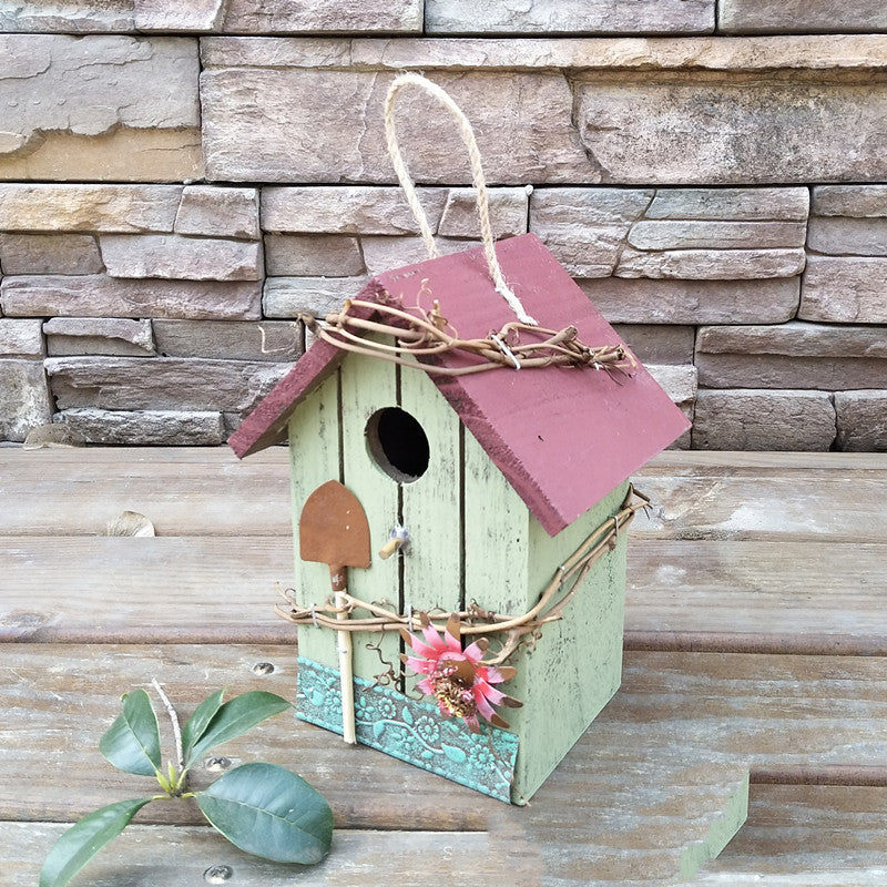 Mintgrüner Nistkasten aus Holz mit rosa Dach und Blumenranken als rustikale Gartendeko