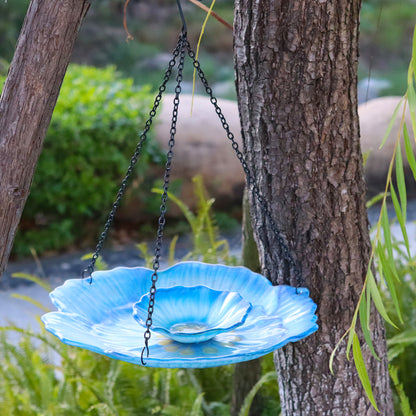 Zweistufige Vogeltränke aus hellblauem Glas in Blütenform hängt an einem Gartenbaum