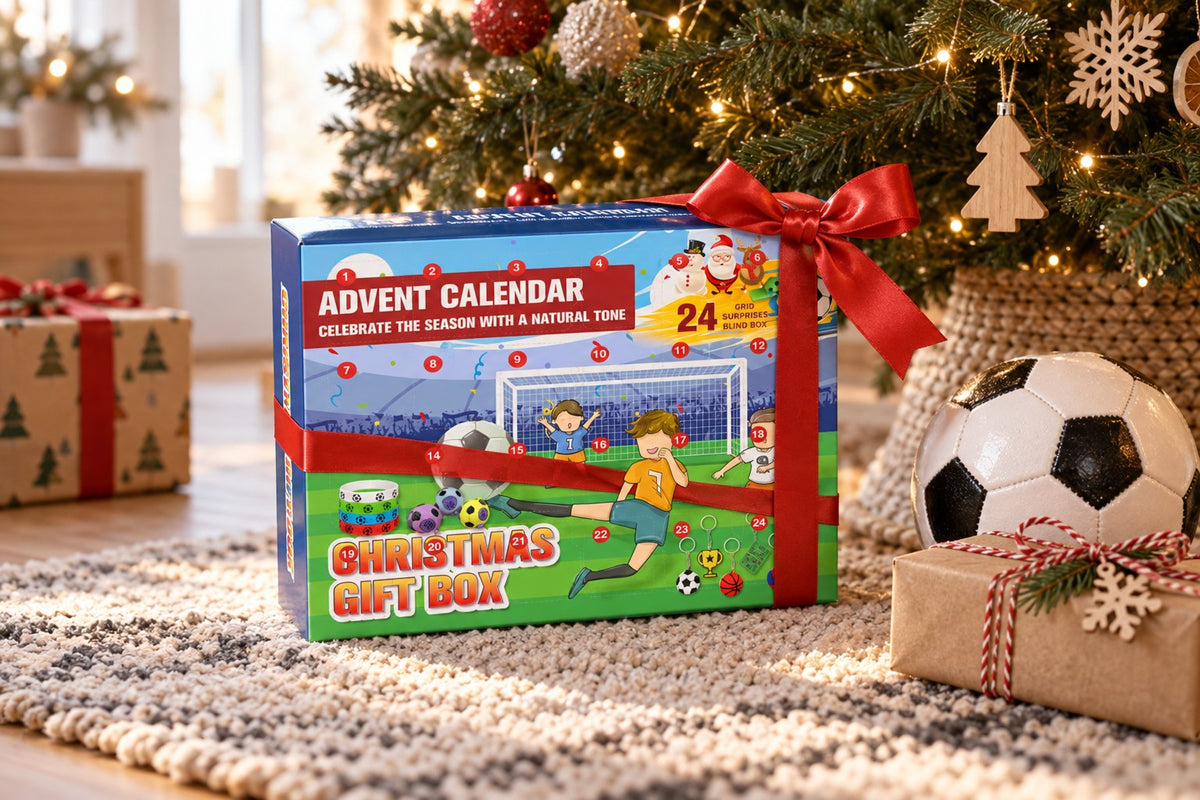 Grün-blaue Fussball-Kalenderbox „Christmas Gift Box“ mit rotem Band unter dem Christbaum, daneben ein Lederball