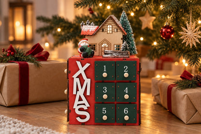 XMAS-Würfel mit grünen Schubladen und Holzhäuschen auf dem Boden zwischen Päckchen in Packpapier