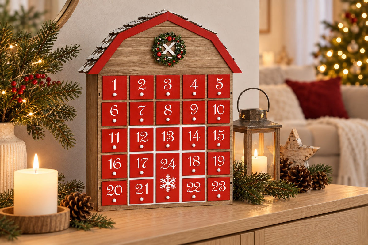 Holz-Adventskalender Scheune auf einem Sideboard neben Kerze, Laterne und Tannenzweigen