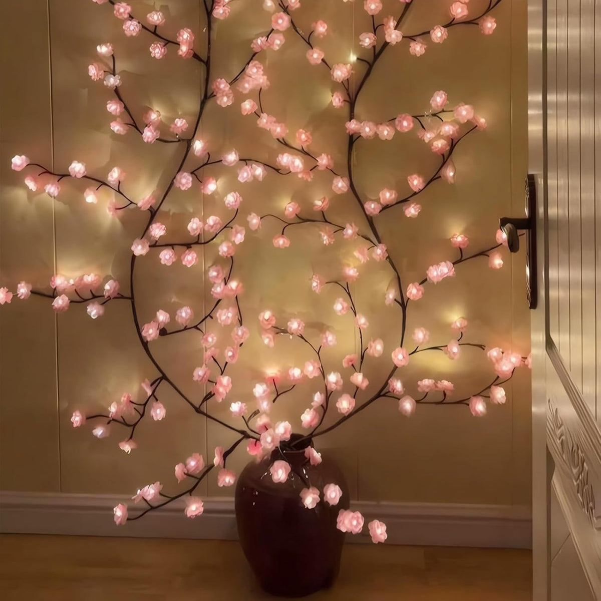 LED Kirschblütenzweig aus einer dunklen Bodenvase an der Wand ausgebreitet