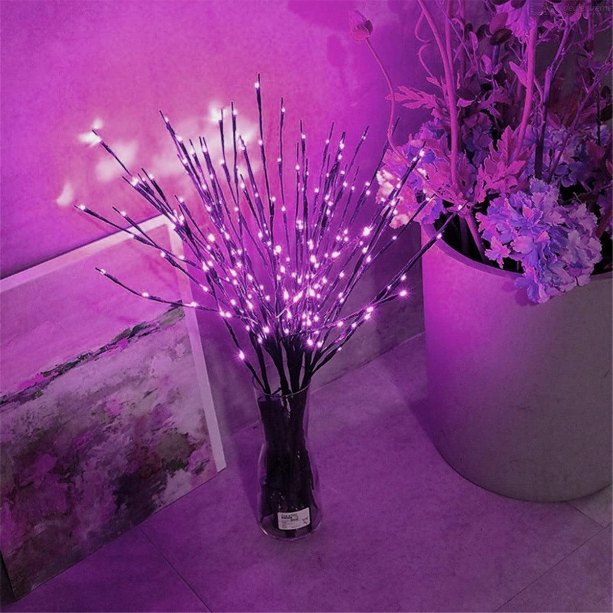 Leuchtzweige mit rosa Licht in einer Glasvase neben Blumen