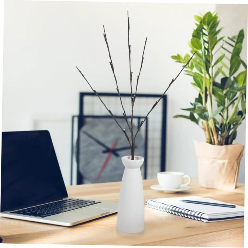 Leuchtzweige in einer weissen Vase auf dem Schreibtisch neben Laptop und Pflanze