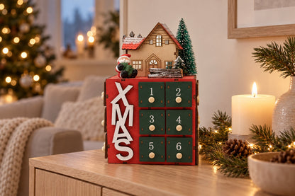 Roter Holz-Adventskalender in Würfelform mit Häuschen und Tanne auf einer Kommode neben einer Kerze