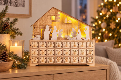 Beleuchteter Krippen-Adventskalender aus Holz auf einer Kommode neben Kerze und Tannenzweigen