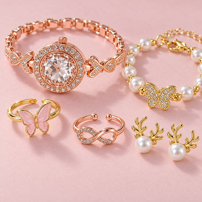 Auf rosa Karton: roségoldene Uhr mit Strass, Perlenarmband mit Schmetterling, zwei Ringe und Rentier-Ohrstecker mit Perle